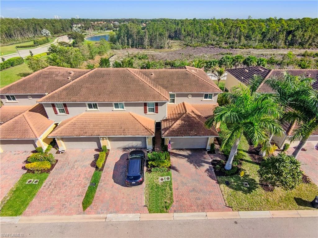 Townhome property featuring a tile roof, brick paver driveway, attached garage, and mature palm trees