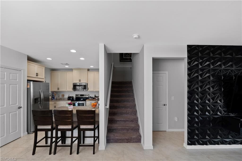 Open concept living area featuring a kitchen with light-toned cabinetry and stainless steel appliances, a multi-level island with seating, and a carpeted staircase