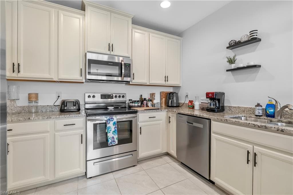 Modern kitchen featuring white cabinetry, stainless steel appliances, granite countertops, and tile flooring