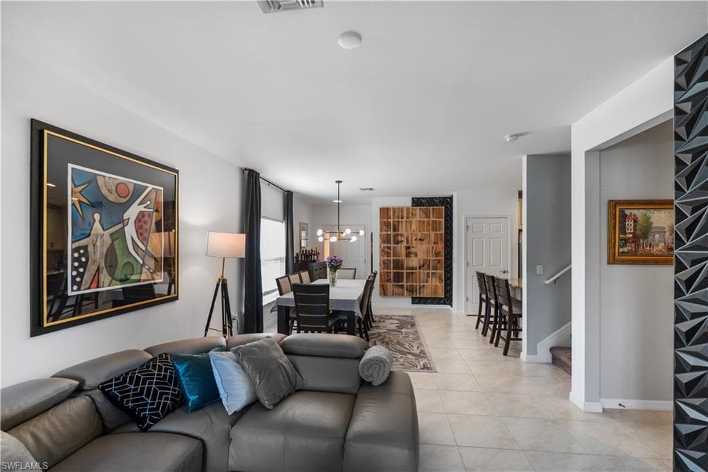 Open-concept interior featuring light-toned tile flooring, a dining area with a linear pendant light fixture, a breakfast bar with seating, a white paneled door, and a staircase with a white handrail