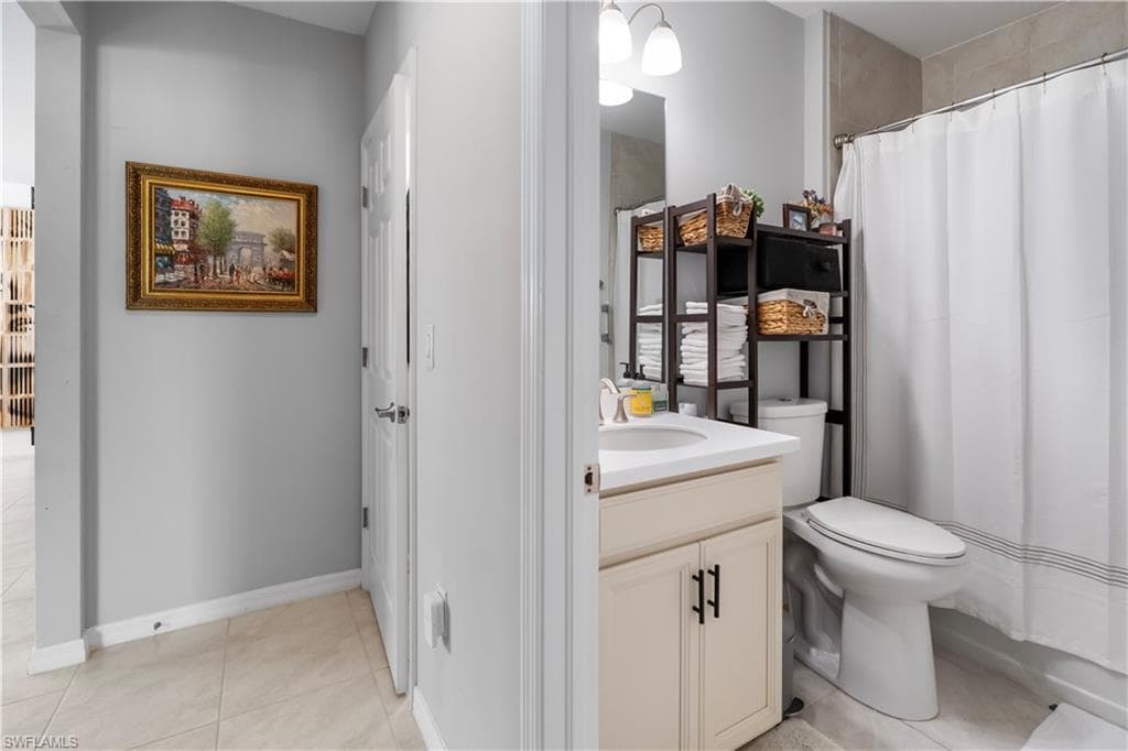 Bathroom with light tile flooring, a single vanity with a white countertop and undermount sink, and a shower with a white curtain and tiled surround