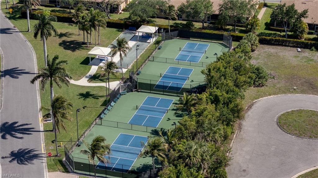 Multiple green tennis courts with blue playing areas, surrounded by fencing and mature landscaping
