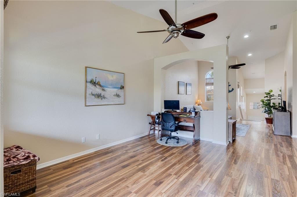 Vaulted ceiling with a ceiling fan, wood-finish flooring, and arched architectural details