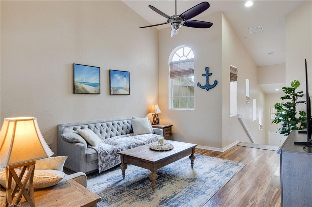 Spacious living area featuring high vaulted ceilings, wood-finish flooring, and an arched window with detailed muntins