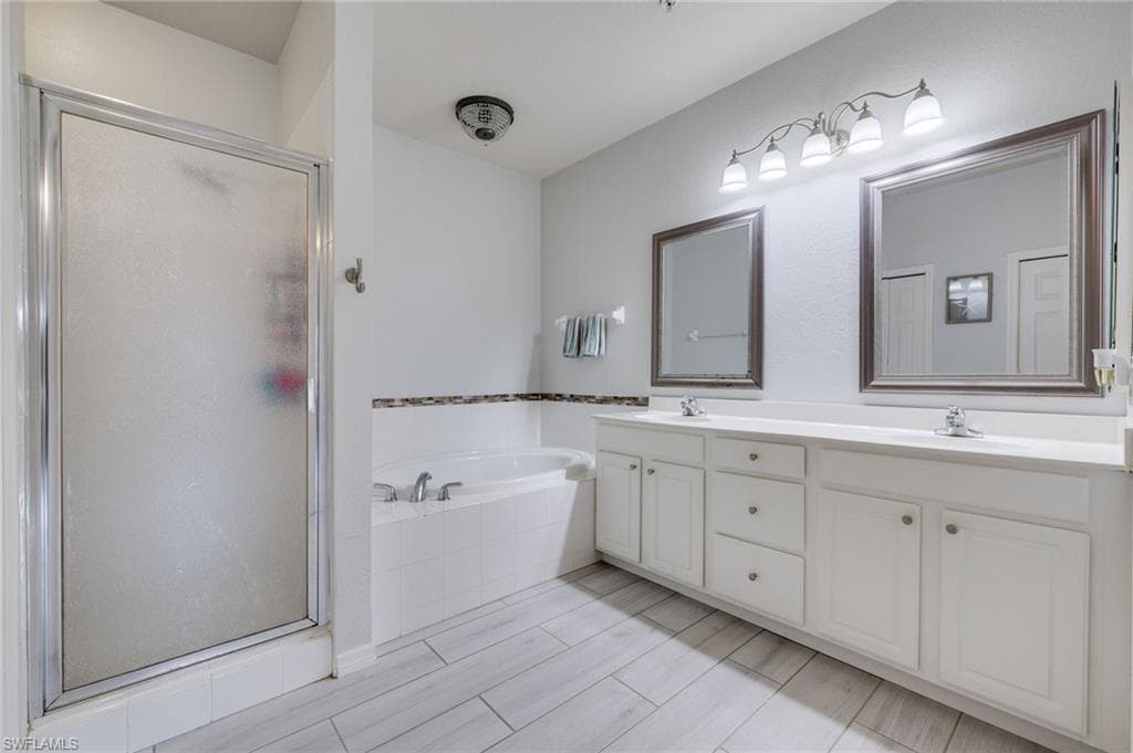 Spacious bathroom featuring a dual vanity with white cabinetry, a built-in soaking tub, a separate shower with a frosted glass enclosure, and light wood-finish plank flooring