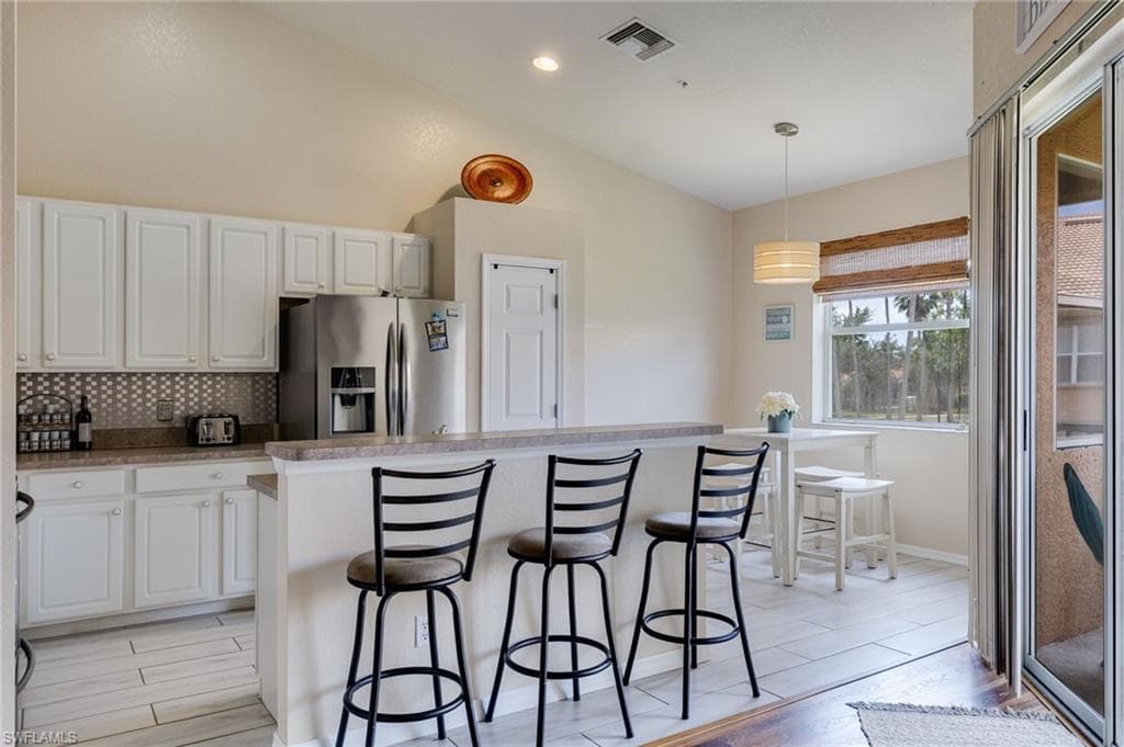 Kitchen featuring white shaker-style cabinetry, stainless steel appliances, a breakfast bar, and a patterned tile backsplash