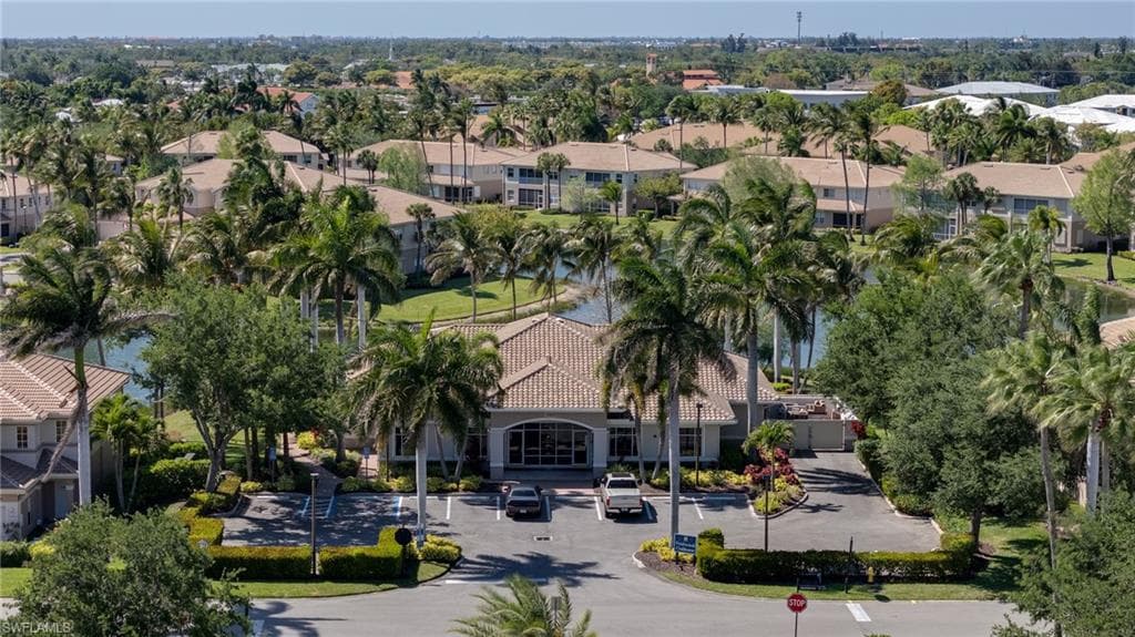 Community entrance featuring a circular driveway, mature palm trees, and manicured landscaping