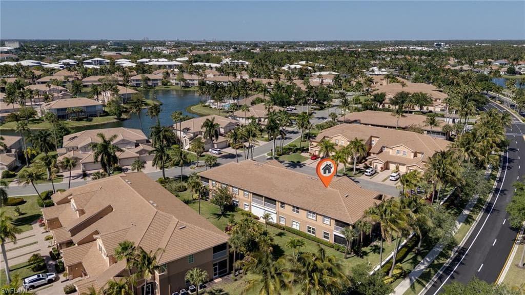 Multi-story residential building with tile roofing and light-colored exterior, surrounded by mature palm trees and green landscaping