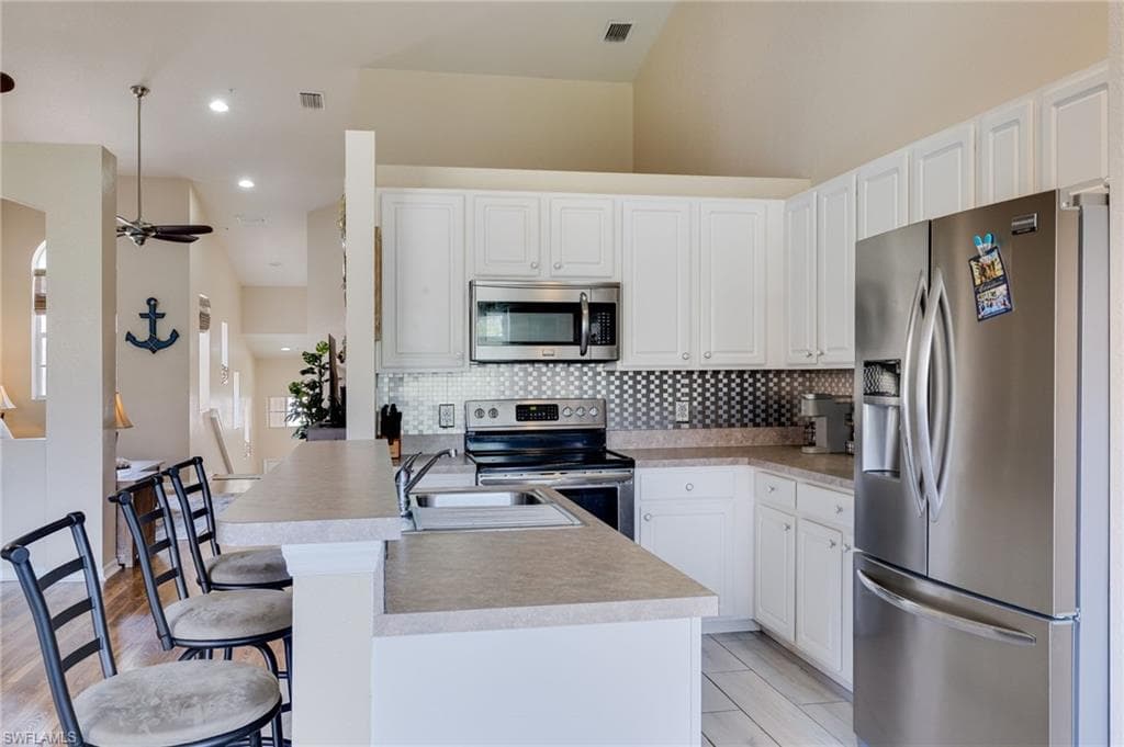 Kitchen featuring white cabinetry, stainless steel appliances, a bar-height counter, a mosaic tile backsplash, and light-toned countertops