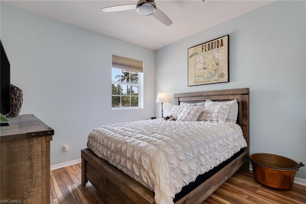 Bedroom featuring wood-finish flooring, a window with outdoor tree scenery, and a ceiling fan