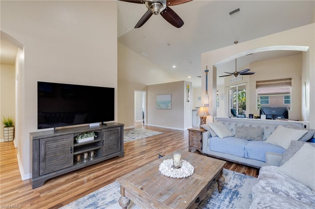 Vaulted ceilings enhance this living area featuring wood-finish flooring, ceiling fans, and an arched entryway
