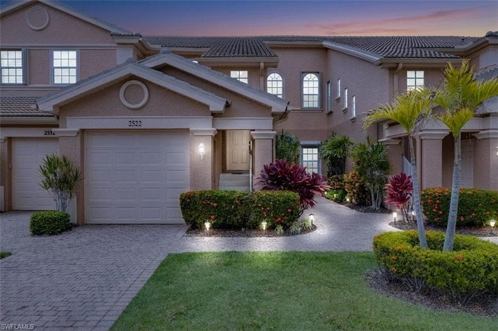 Townhome featuring an attached garage, paver driveway, and tiled roof