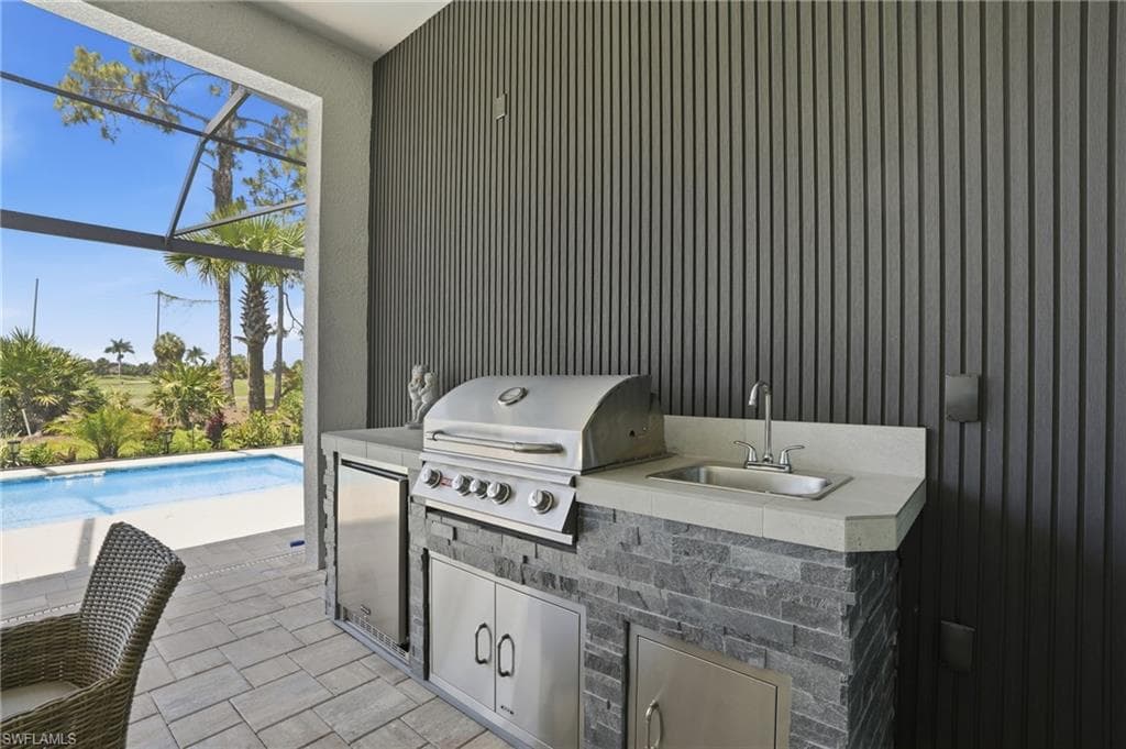 Outdoor kitchen featuring a stainless steel grill, integrated sink, and undercounter refrigeration