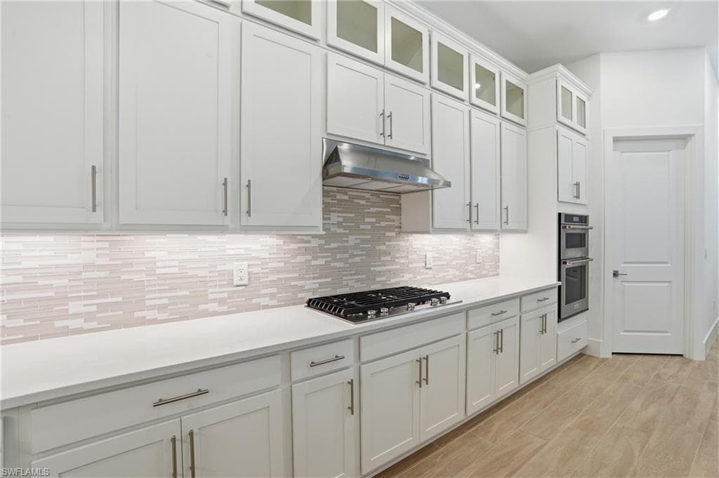 Kitchen featuring extensive white cabinetry, a built-in stainless steel double oven, a gas cooktop, light-colored countertops, and wood-finish flooring