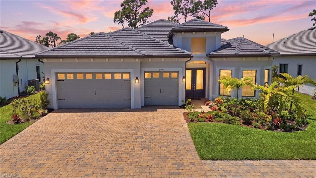 Modern stucco exterior with a tile roof, featuring a paver driveway, an inviting entry with double doors, and a meticulously landscaped front yard
