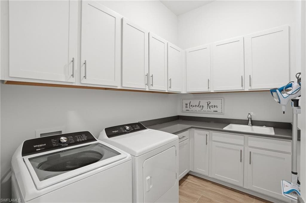Utility room featuring extensive white shaker-style cabinetry, dark countertops, a rectangular undermount sink with a chrome faucet, and wood-finish flooring