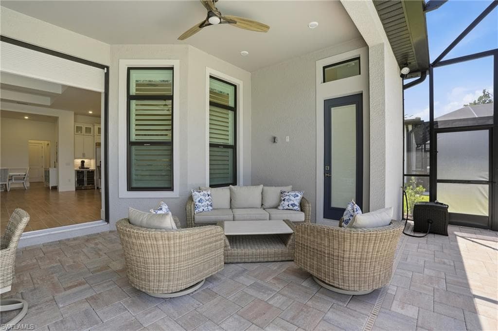Screened outdoor living area featuring a ceiling fan, bay window with louvered panels, a full-lite exterior door, and large format paver flooring