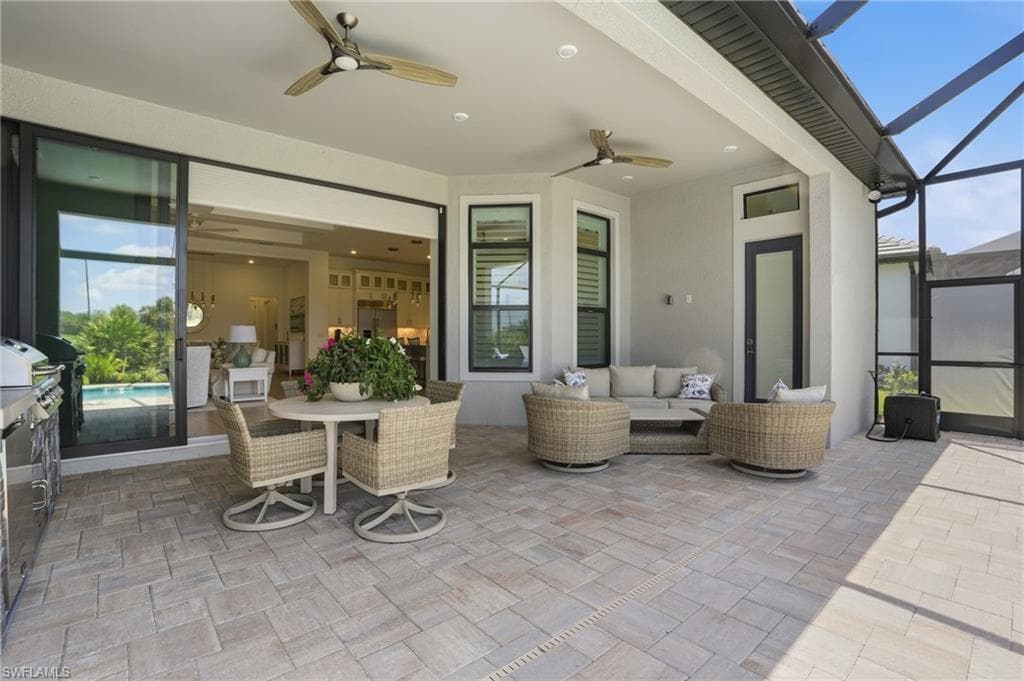 Expansive covered patio featuring paver flooring, two ceiling fans with integrated lighting, and multiple access points