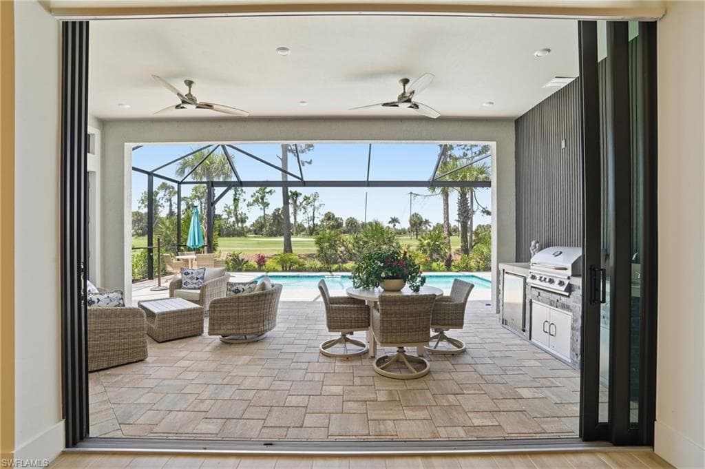 Expansive covered patio featuring patterned paver flooring, a built-in outdoor kitchen with grill, and ceiling fans