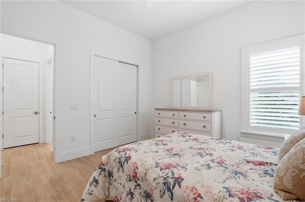 Bright interior featuring wood-finish flooring, a window with white louvered shutters, and a closet with bifold doors