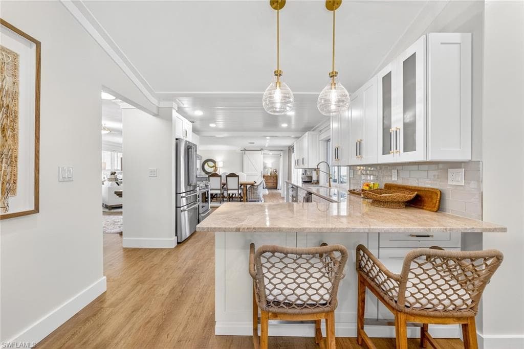 Kitchen featuring a breakfast bar with stone-finish countertop, white cabinetry with gold-tone hardware, stainless steel appliances, and wood-finish flooring