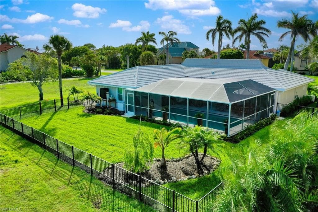 Expansive fenced backyard featuring a screened-in pool enclosure, mature palm trees, and an established garden bed