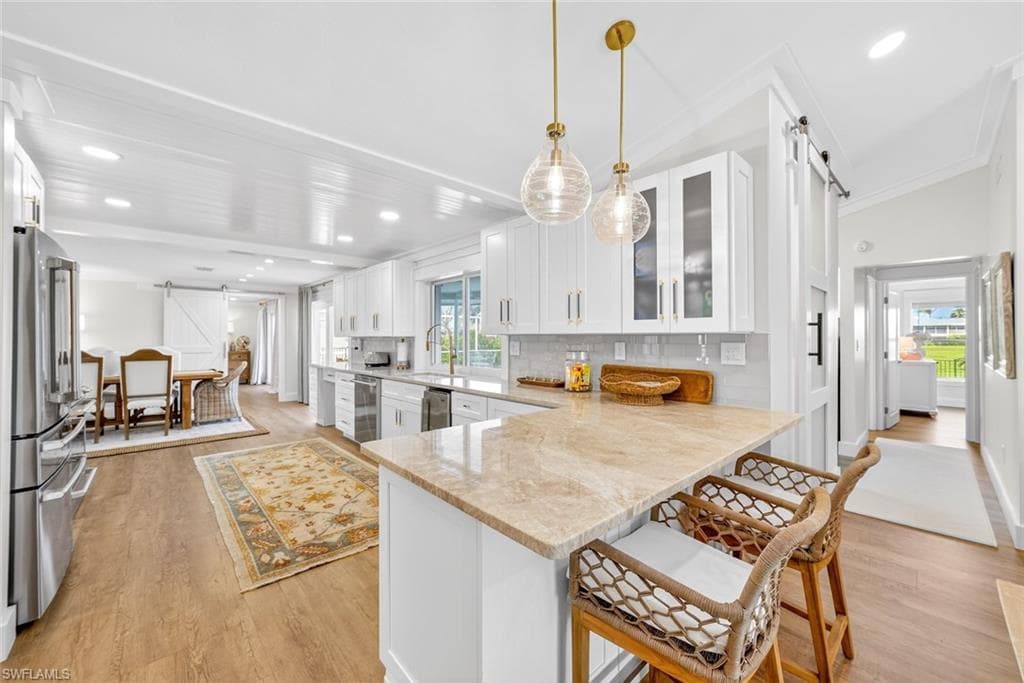 Open-concept kitchen featuring an island with stone countertop, white shaker cabinetry, stainless steel appliances, and wood-finish flooring