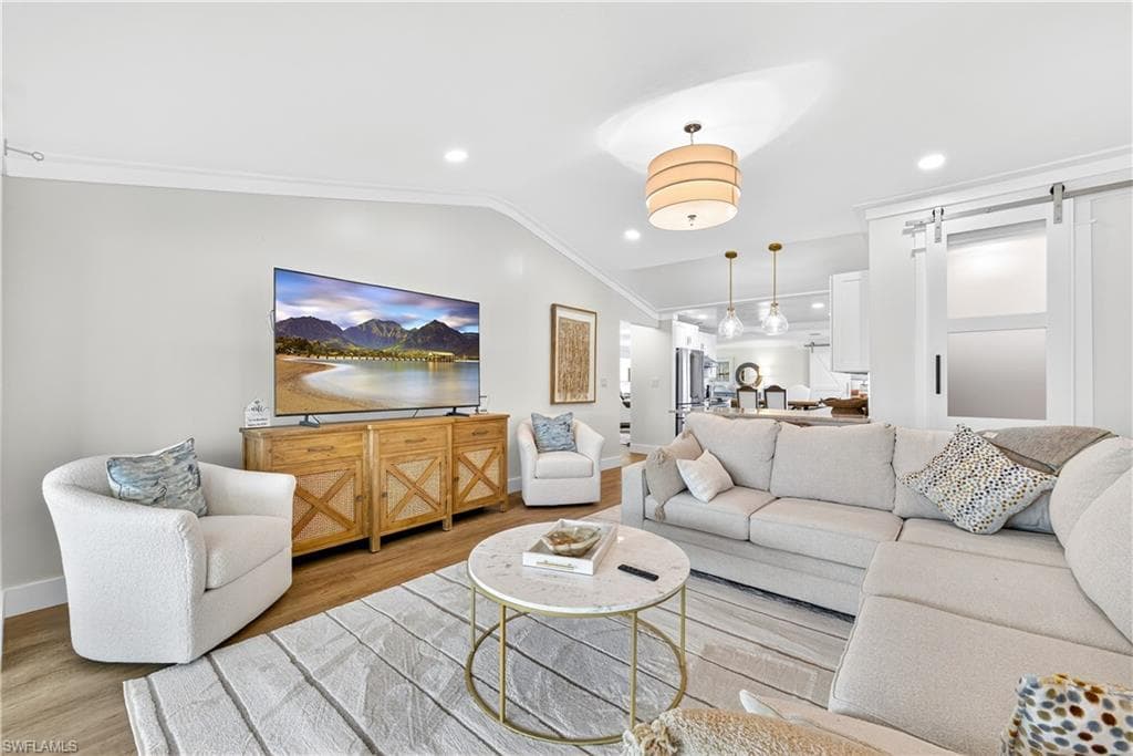 Spacious living area featuring vaulted ceilings, recessed lighting, wood-finish flooring, a contemporary drum pendant light, and a white barn door
