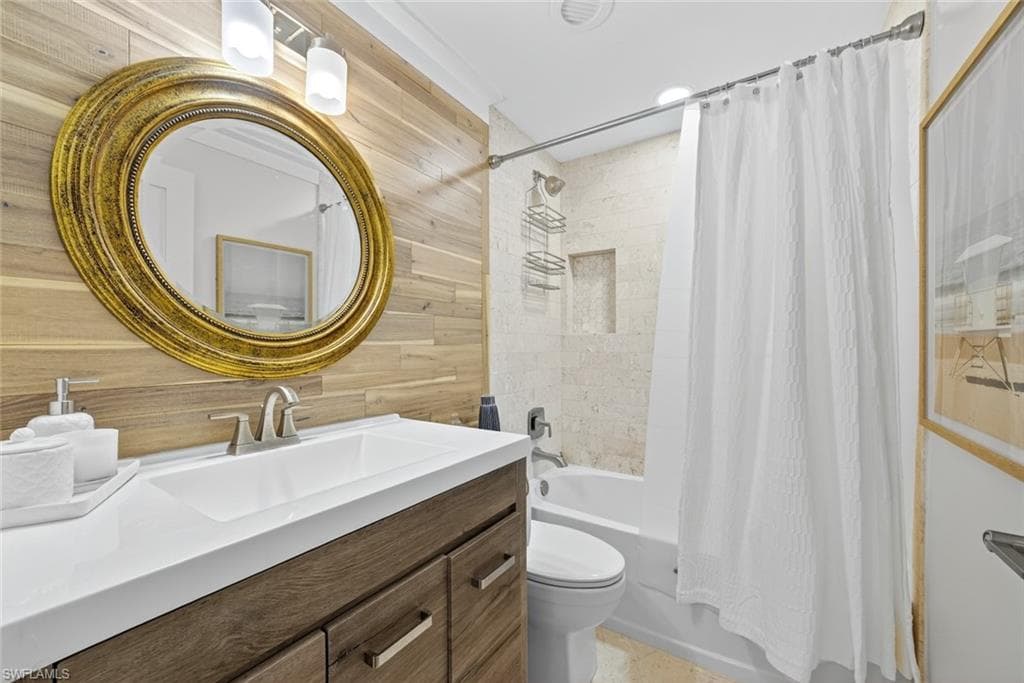 Bathroom featuring a wood-panel accent wall, oval mirror with an ornate gold frame, and a vanity with wood-finish cabinetry