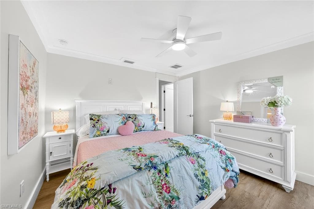 Bedroom with wood-finish flooring, white walls, and crown molding