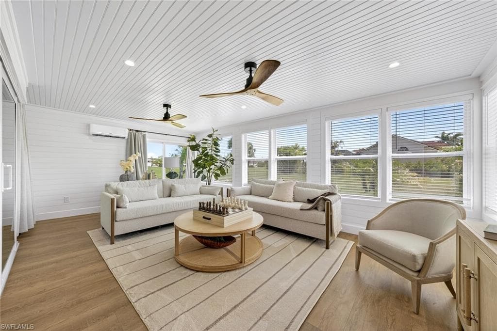 Sun-filled living area featuring wood-finish flooring, white shiplap walls, multiple windows with blinds, recessed lighting, and two ceiling fans
