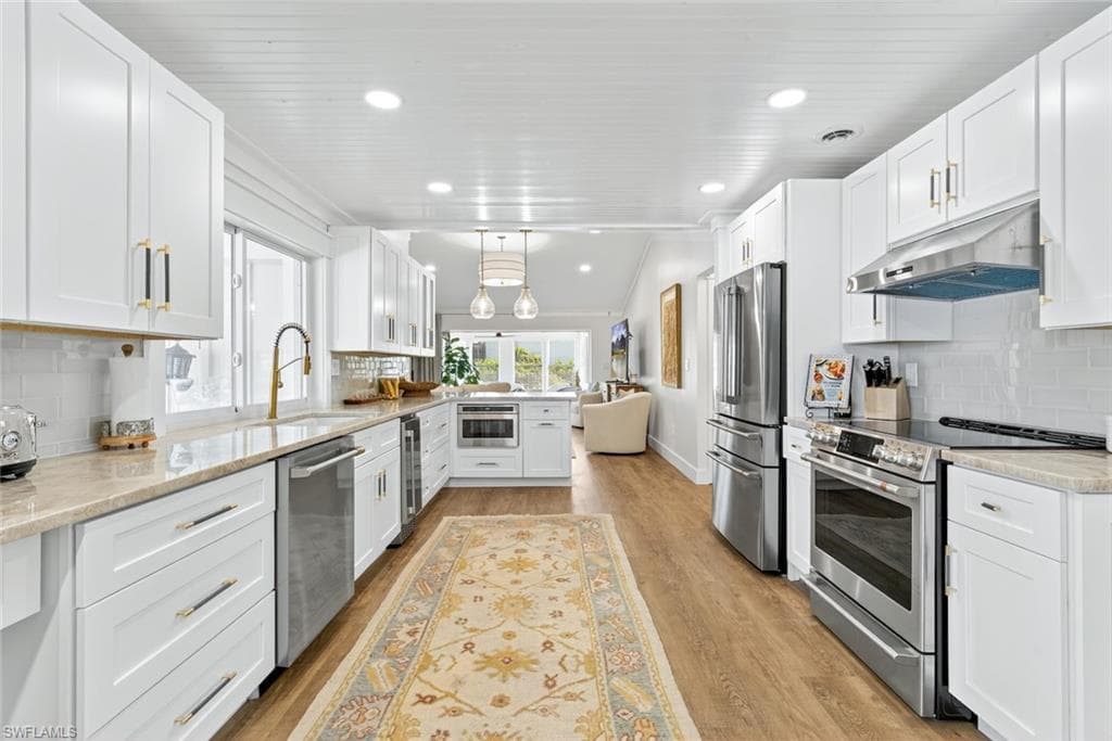 Bright kitchen featuring white shaker cabinetry, stainless steel appliances, granite-style countertops, and wood-finish flooring