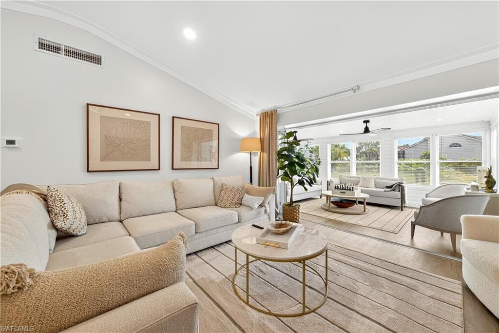 Spacious living area featuring vaulted ceilings with crown molding, wood-finish flooring, and ample natural light from multiple windows