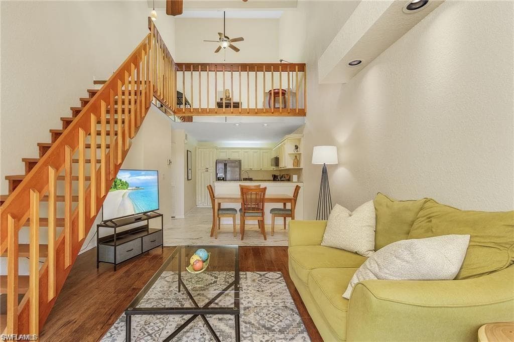 Living area with stairway, wood finished floors, a high ceiling, and ceiling fan