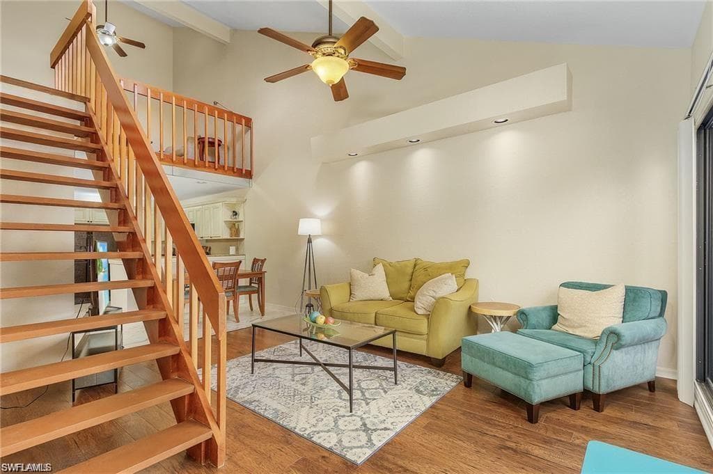 Living area featuring beamed ceiling, wood finished floors, ceiling fan, and stairs