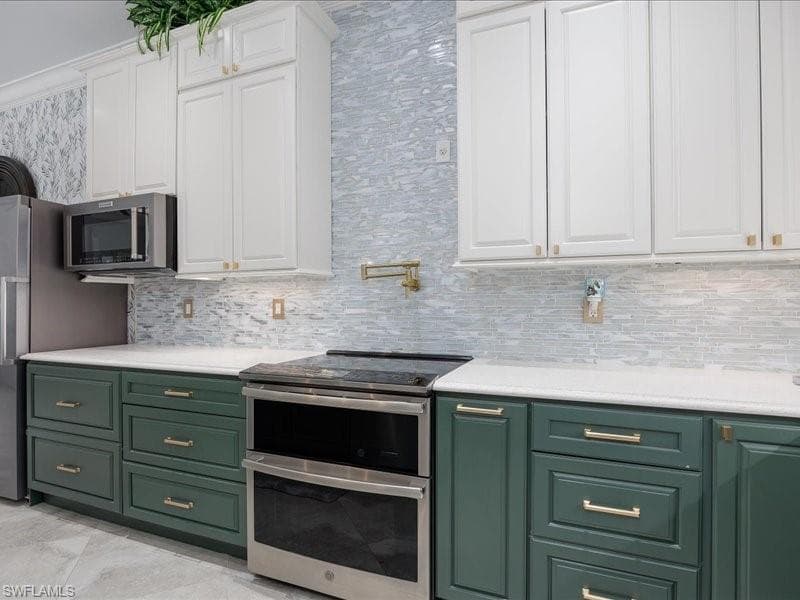 Kitchen featuring two-tone cabinetry with white upper cabinets and green lower cabinets, stainless steel appliances, white countertops, and a full-height tile backsplash with a linear pattern