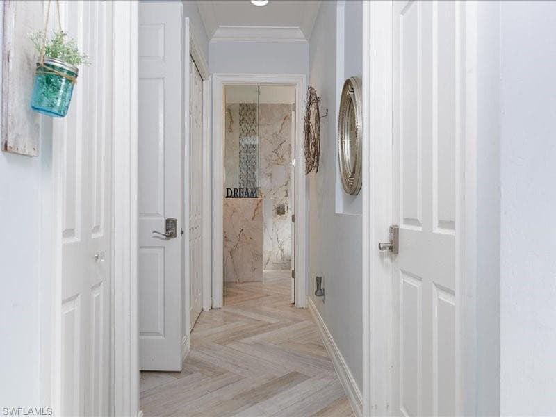 Hallway featuring wood-finish flooring in a herringbone pattern, white paneled doors with brushed nickel hardware, and light-toned wall paint