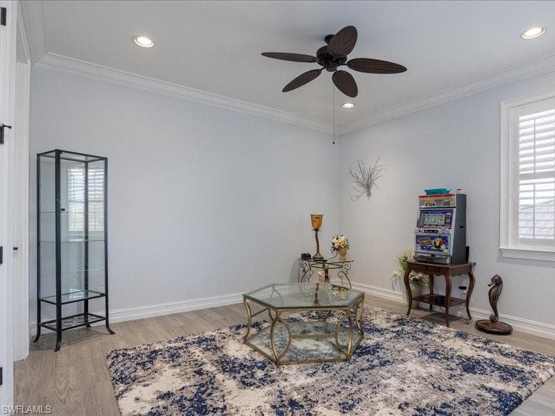 Bright interior space featuring wood-finish flooring, a ceiling fan, recessed lighting, crown molding, and plantation shutters
