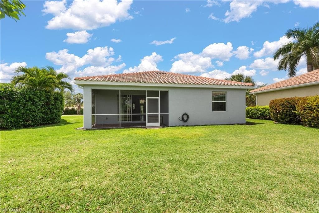 Rear exterior view of the single family story residence with screened lanai, tile roof, and expansive green lawn.