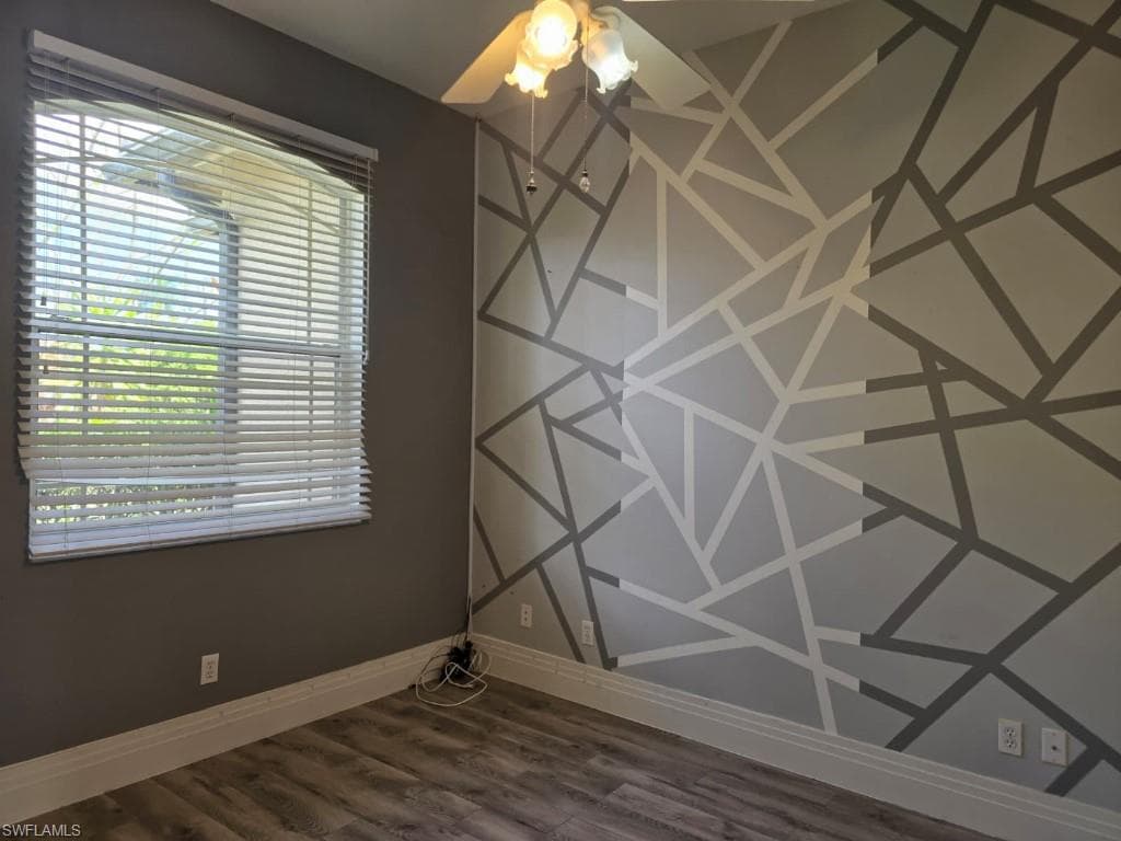 Room featuring a geometric accent wall, wood-finish flooring, and a ceiling fan with integrated lighting