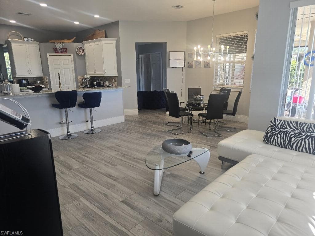 Open-concept living area featuring wood-look tile flooring, a kitchen island with seating, white shaker-style cabinetry, and a dining area with a modern chandelier