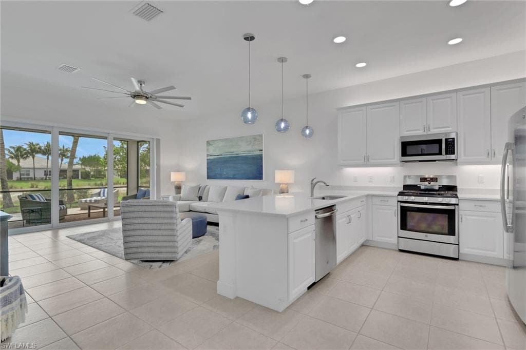 Open-concept living area featuring a white kitchen with stainless steel appliances, a center island with sink, and pendant lighting
