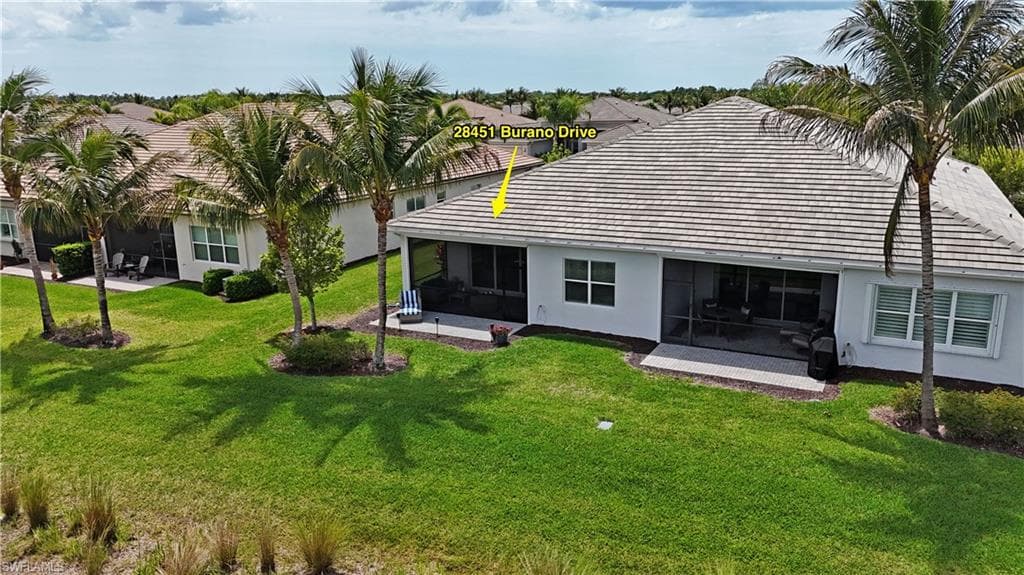 Expansive rear exterior featuring a screened lanai, a large green lawn, and mature palm trees