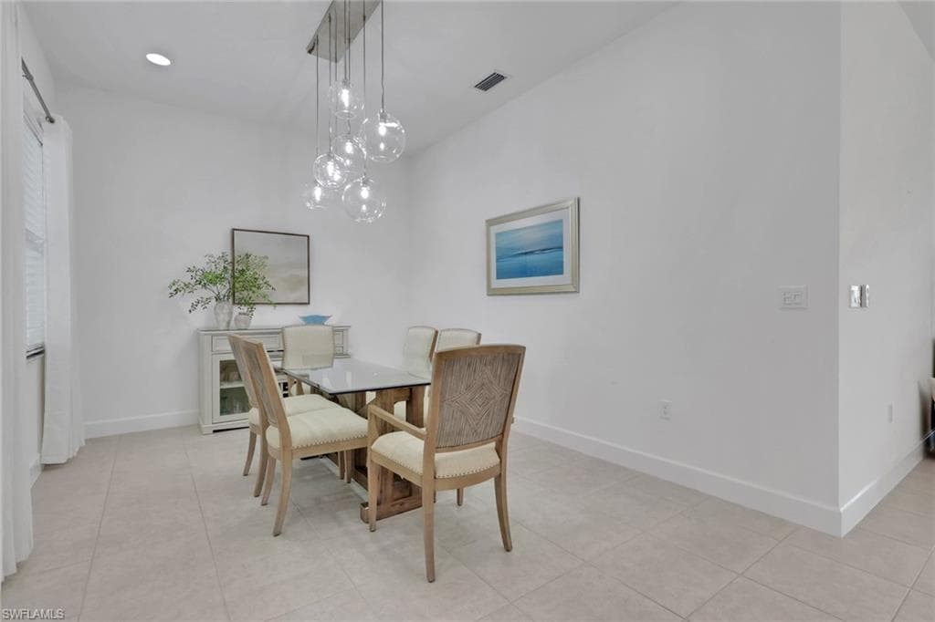 Dining area featuring a contemporary chandelier with multiple glass globes, tile flooring, and crisp white walls