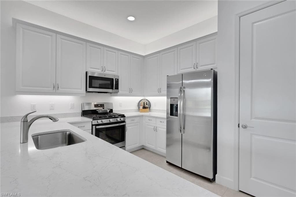 Modern kitchen featuring white shaker cabinetry, stainless steel appliances, light-toned countertops, a stainless steel sink with a gooseneck faucet, and recessed lighting