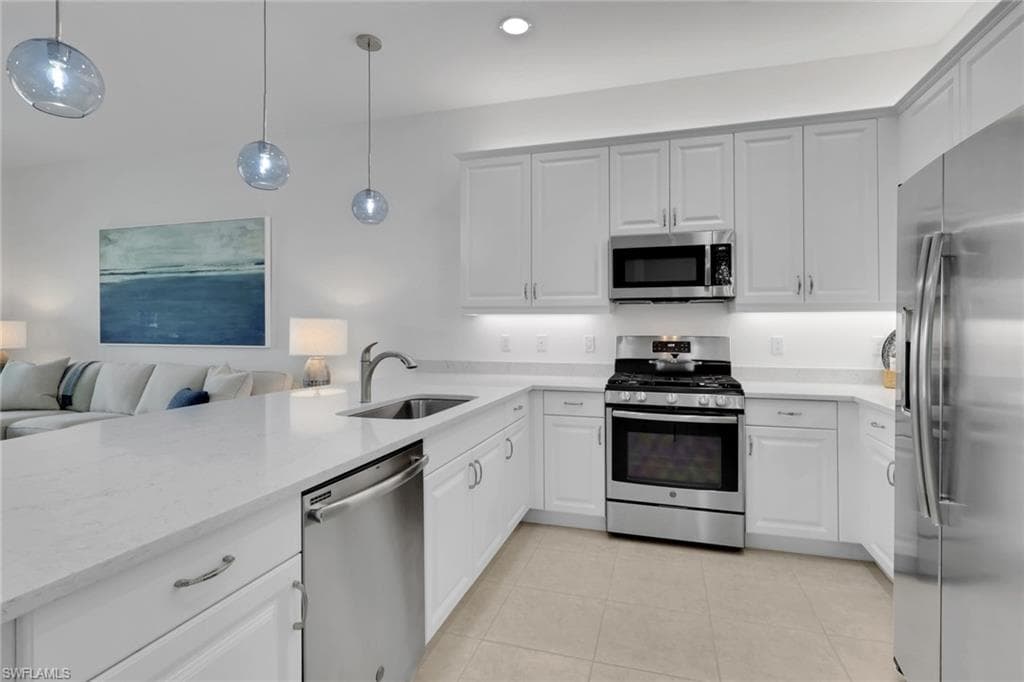 Modern kitchen featuring white cabinetry, stainless steel appliances, light countertops, a stainless steel sink with a gooseneck faucet, and integrated under-cabinet lighting