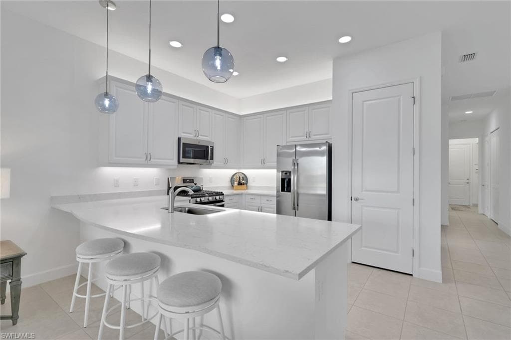 Modern kitchen featuring white shaker cabinetry, stainless steel appliances, a white solid surface countertop, and three spherical pendant lights