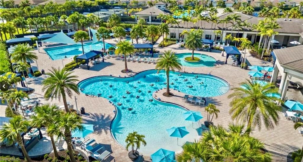 Resort-style pool area featuring multiple swimming pools, extensive hardscaping, mature palm trees, and shaded lounging areas