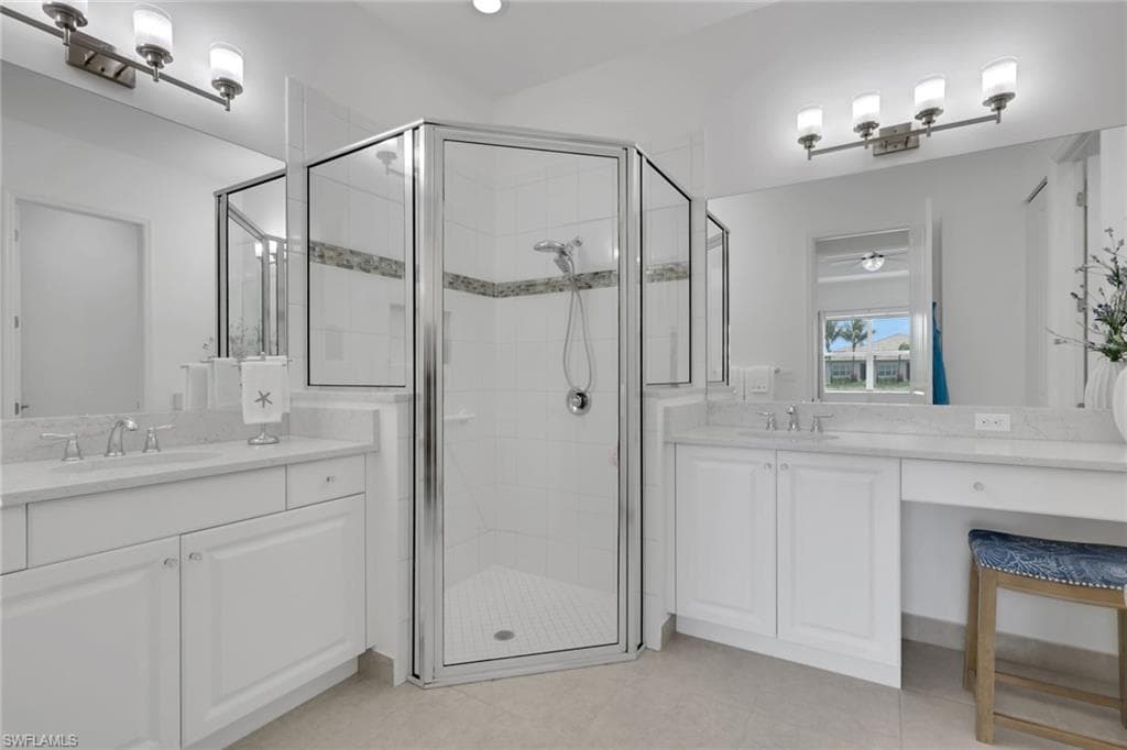Bathroom featuring a glass-enclosed shower with decorative accent tile, dual vanity sinks, white cabinetry, and a dedicated vanity area