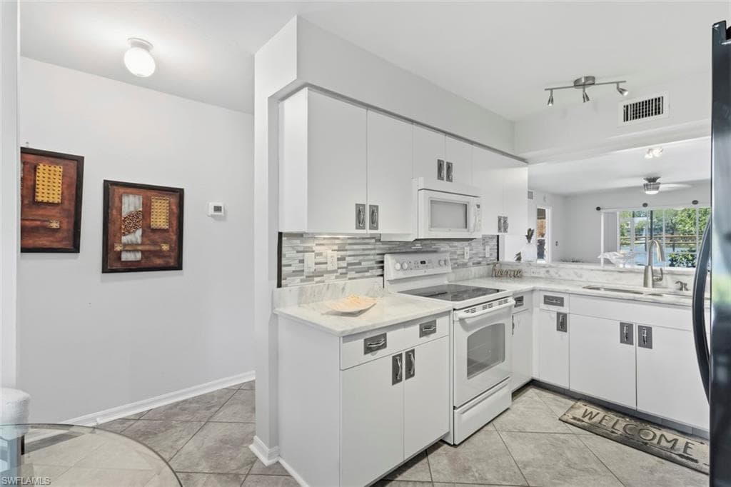 Bright kitchen featuring white cabinetry, light countertops, a tile backsplash, and a pass-through window